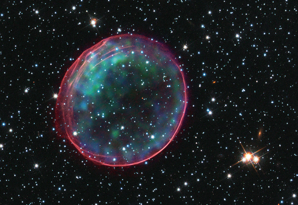 The remnants of a supernova, located in the Large Magellanic Cloud – a satellite galaxy to our Milky Way, 160,000 light years distant. The image combines optical data from the Hubble Space Telescope showing the expanding blast wave in pink, and data from the Chandra space observatory showing x-rays from heated material in green and blue. Photo: NASA/Chandra X-Ray Observatory
